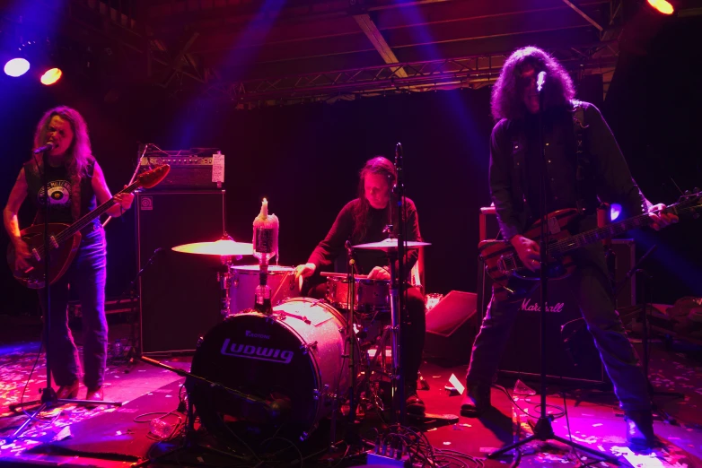 three musicians are performing on stage in front of purple lighting