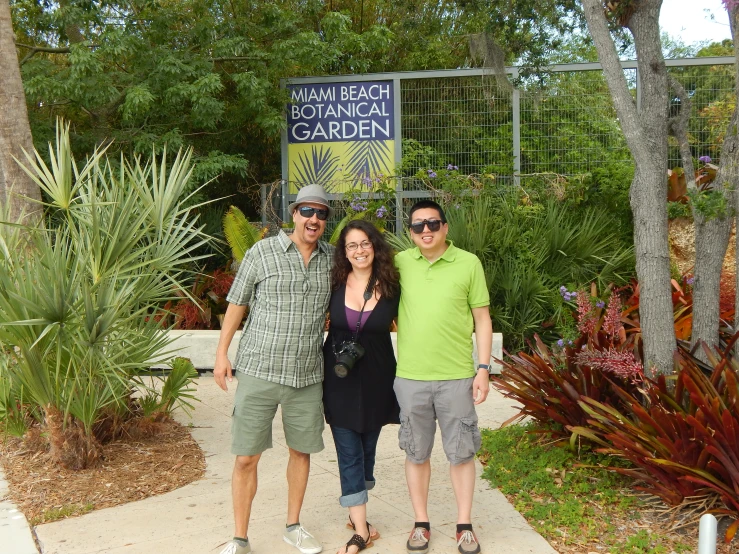 three people smiling for the camera in front of a garden