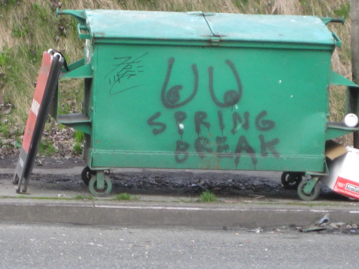 a green garbage container with graffiti on it sitting on a street
