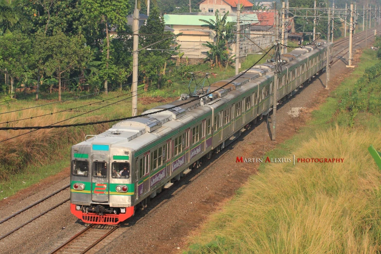 an orange and green train traveling down tracks near a rural area