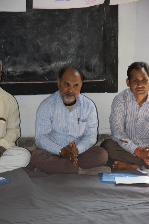 three men are sitting in front of a black board