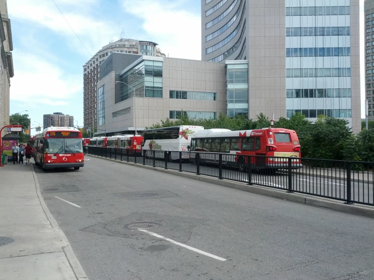 several city buses parked near a fence outside buildings