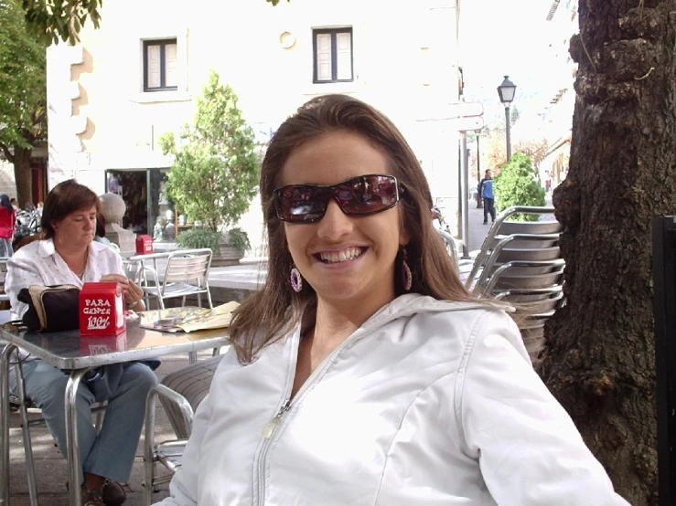 a woman in a white jacket sitting outside smiling