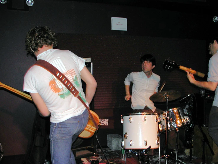 people playing instruments in a room with a wall and a guitar