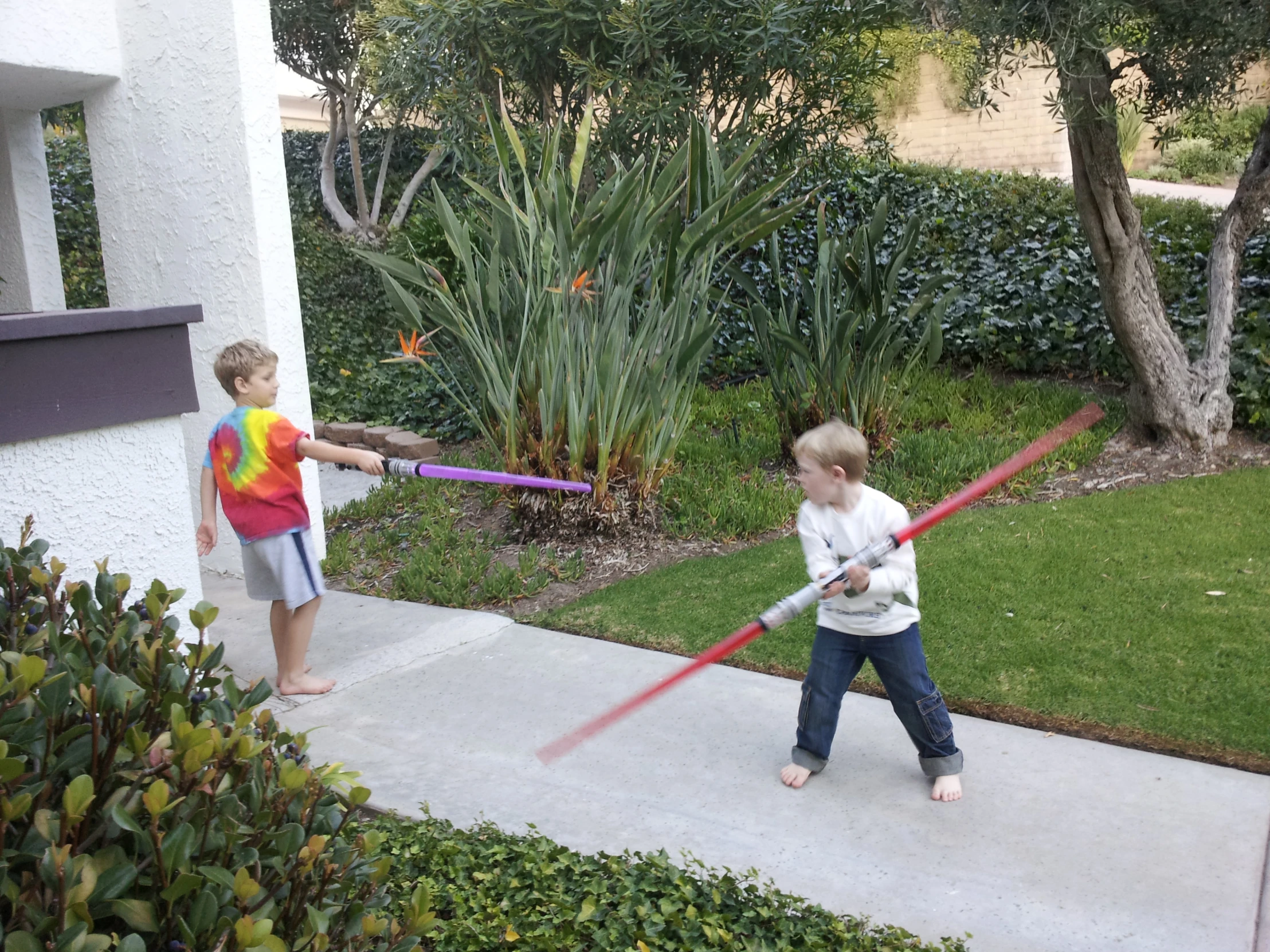 two children playing with plastic swords on the sidewalk