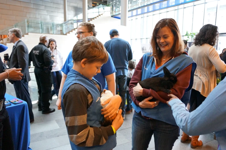 three people standing near a crowd of people one holding a cat while the other holds a baby