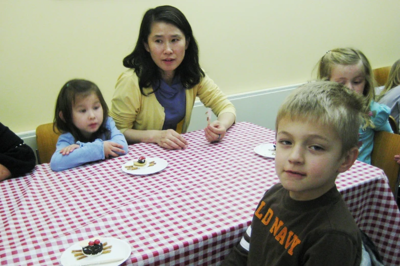 children at a table with food and adults seated behind them