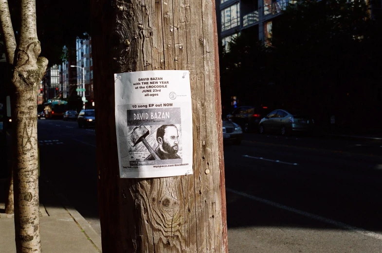 a newspaper ad posted on a tree next to a sidewalk