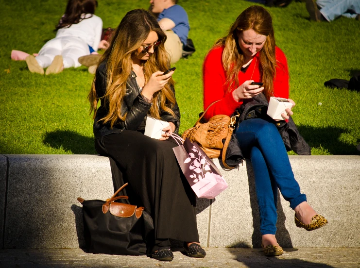 two beautiful young ladies sitting on steps using cell phones