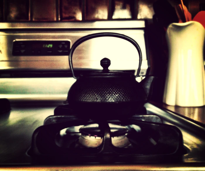 a stove top with a tea kettle on it and pots in the background