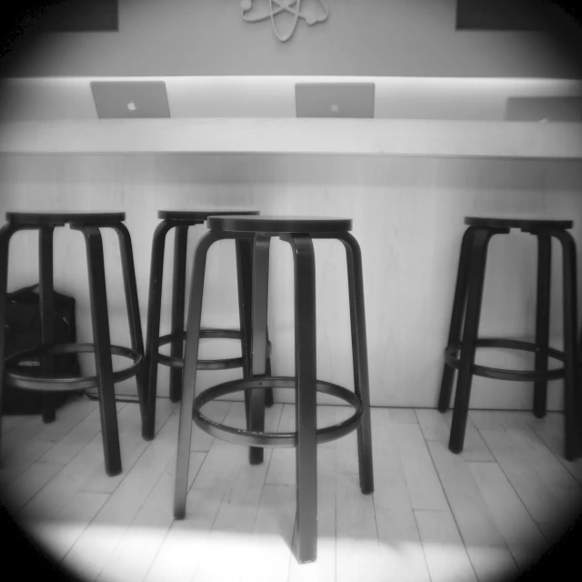 three black stools and one blue chair are against a wall with a clock