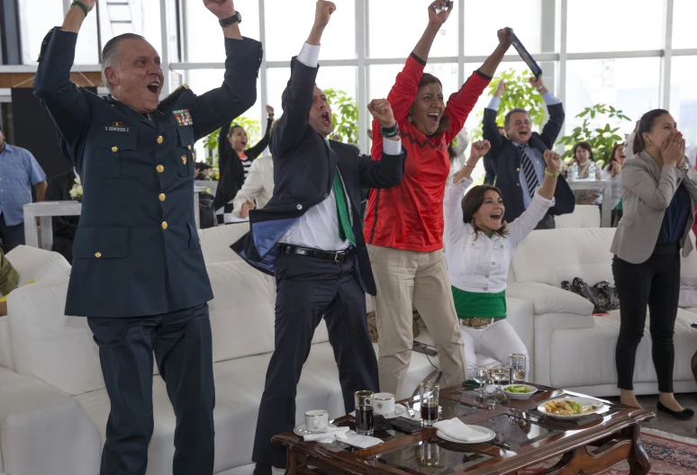 an army officers celetes while in the background sits other women and men, clapping and waving