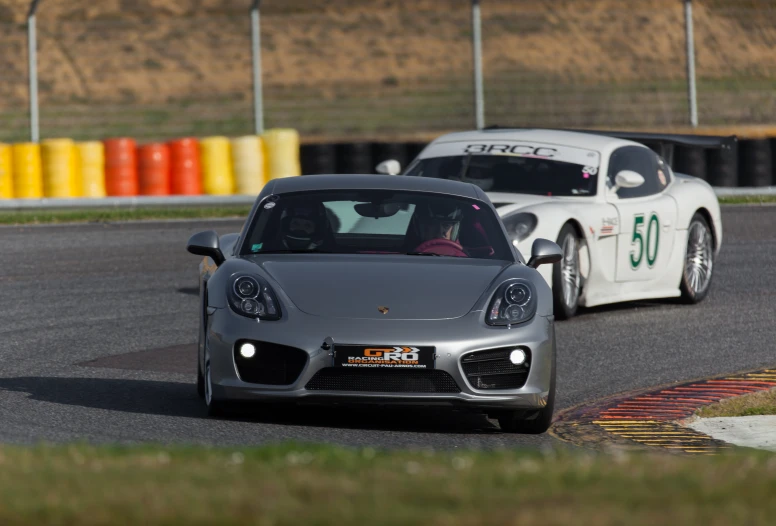 two gray sports cars rounding a track, one going fast