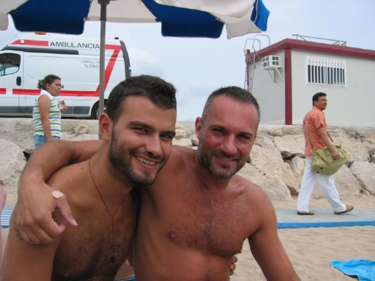 two men sitting in the sand next to a boat