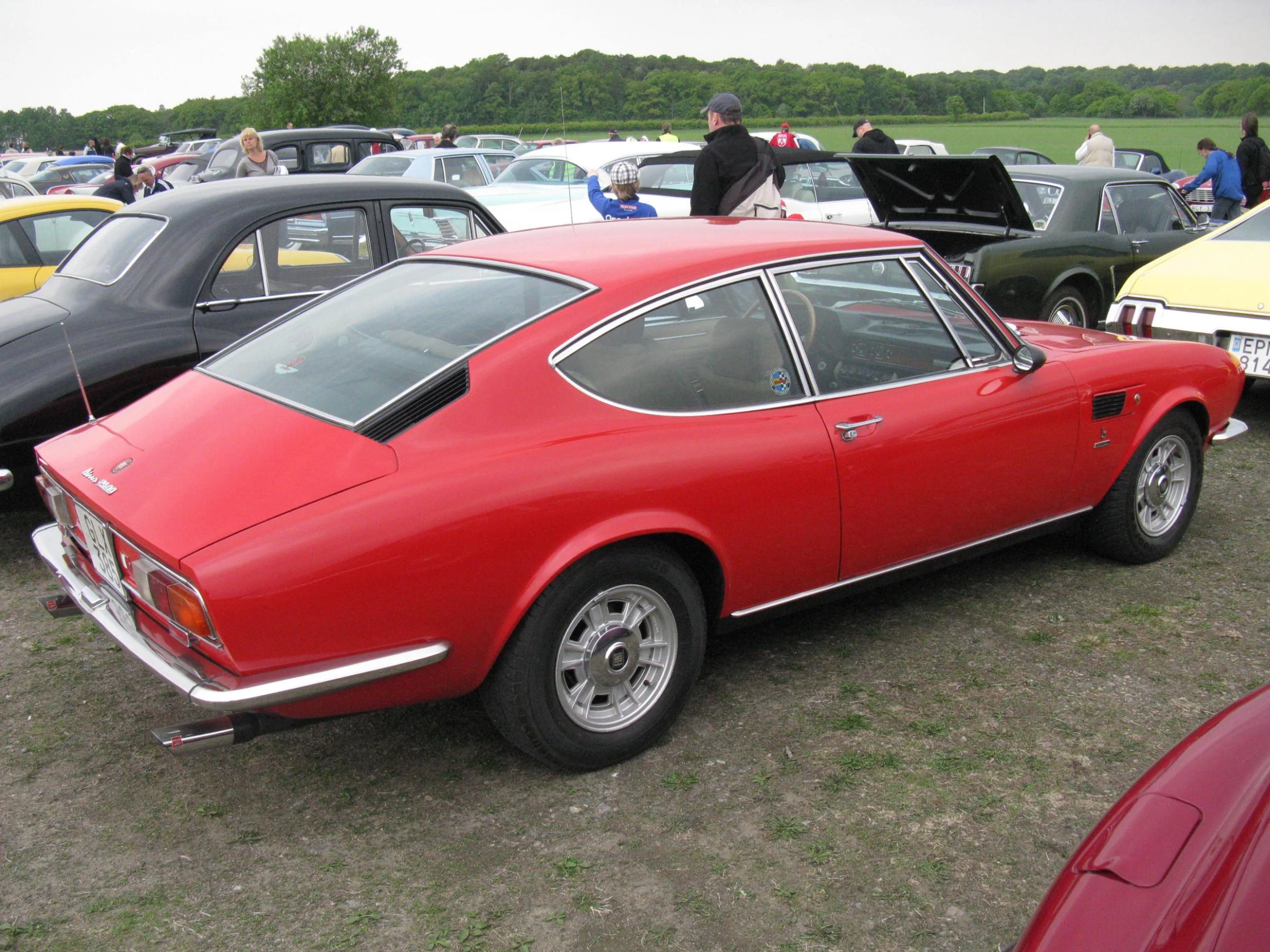 a red sports car sits in a parking lot next to other sports cars