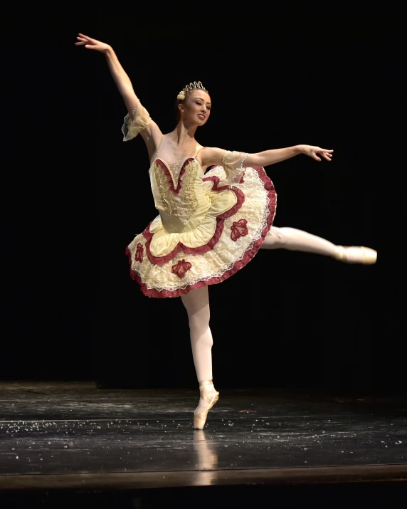 a ballerina dressed in yellow and red tutu with the ballerina holding out one arm