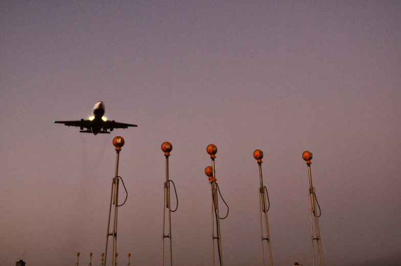 an airplane flying in the sky and over several red, yellow and white light poles