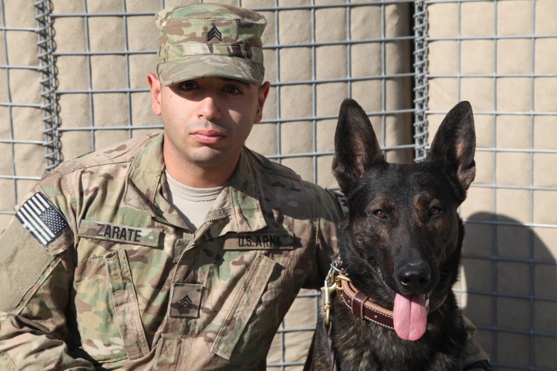 a military man with his dog in front of a fence