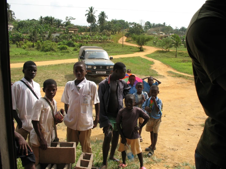 group of children standing outside and waiting to cross a dirt road