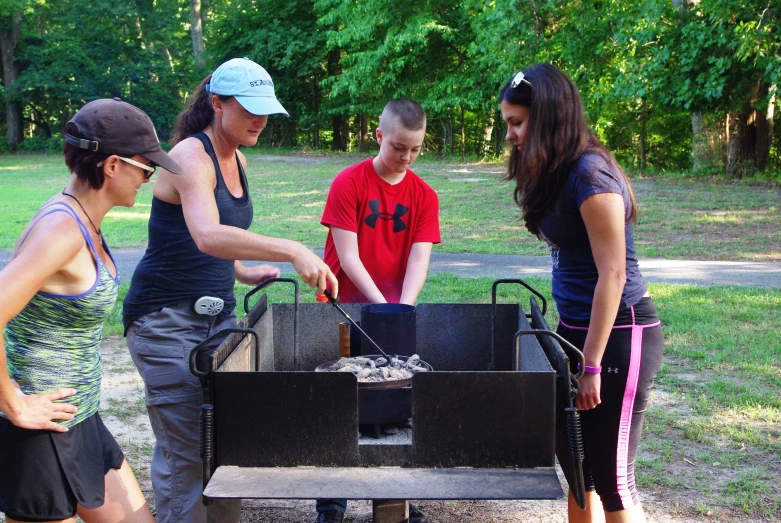 four people are standing around an open grill