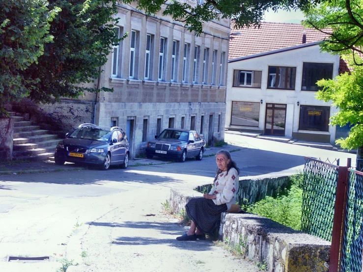 a woman sitting on a cement ledge near some parked cars