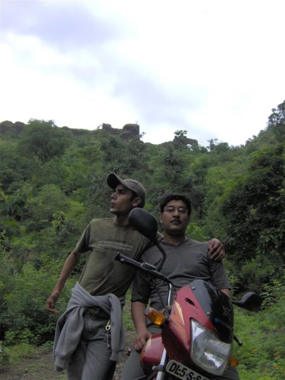 two young men walking towards the camera behind a motorbike