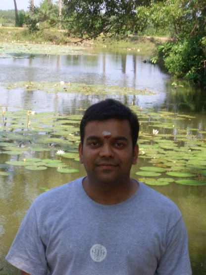 a man standing near water and greenery in the background