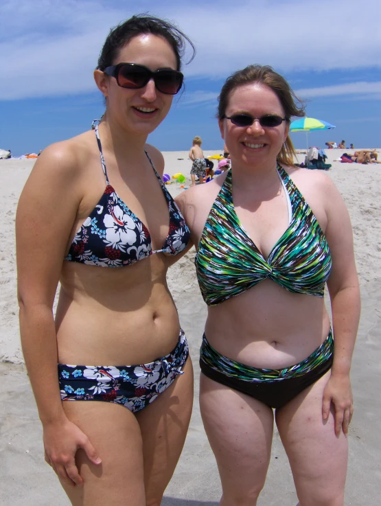 two women in bikinis standing at the beach