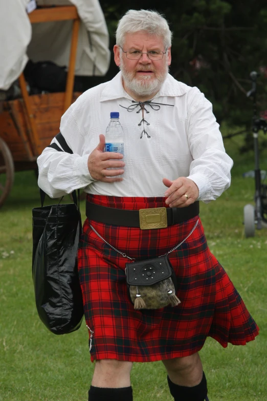 man in scottish kilt holding a bottle and holding a small black bag