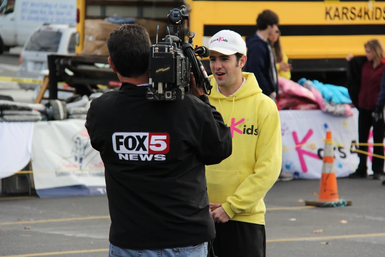 a camera operator and two young men talking in front of a school bus