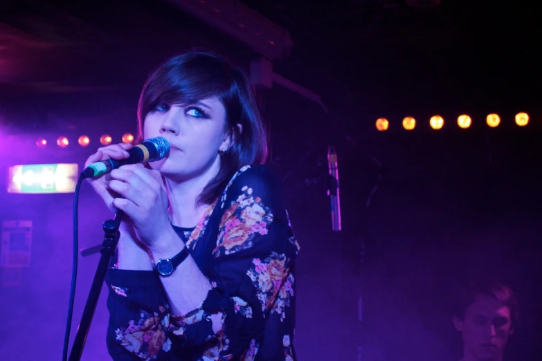 a woman holding a microphone with purple light in the background