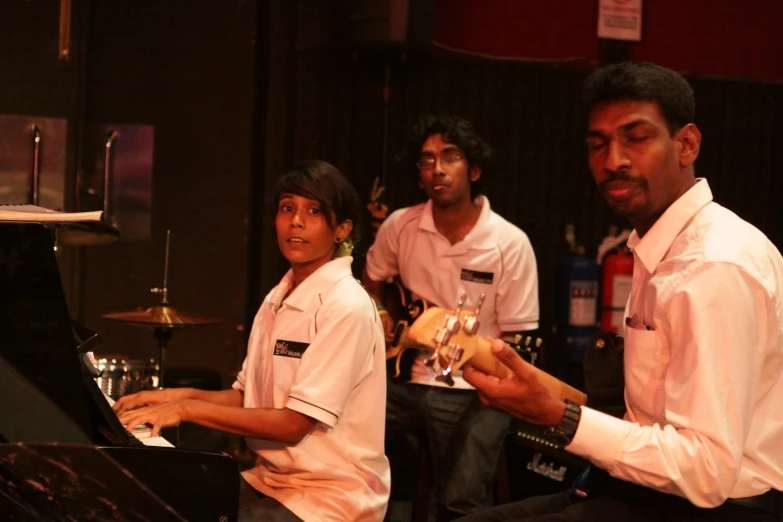 three people in front of a black piano and a man in a white shirt holding a glass