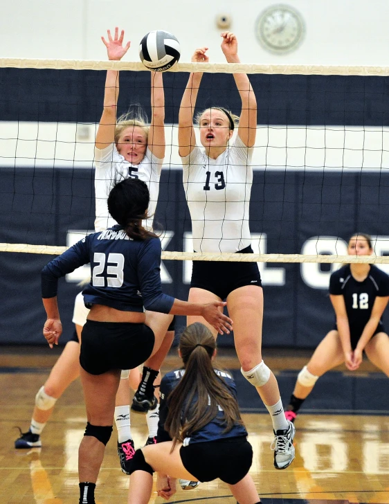 a group of young ladies playing volleyball inside a gym