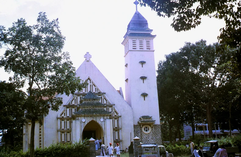 people walk past a large white church with a clock on it