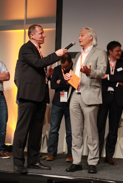 three men in suits speak into microphones on stage