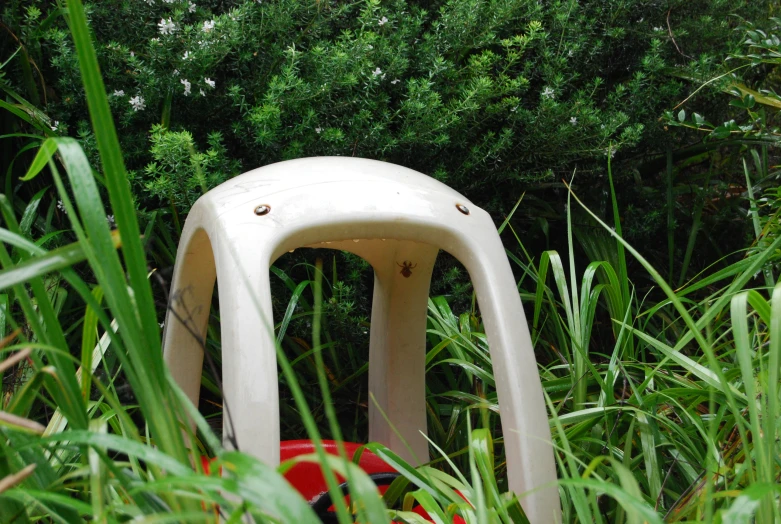 the large white chair is in tall grass near trees