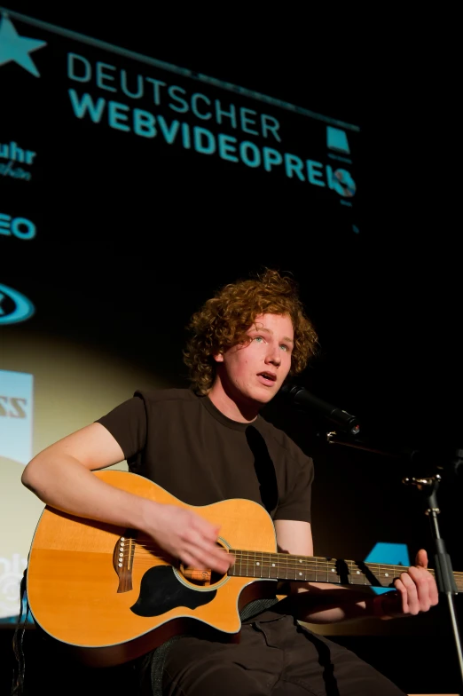 a man with red hair is holding an acoustic guitar