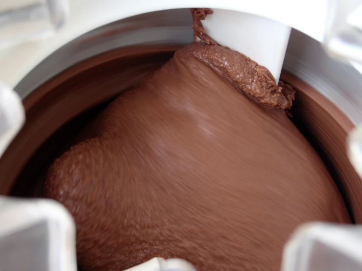 a hand is stirring a chocolate batter in a blender