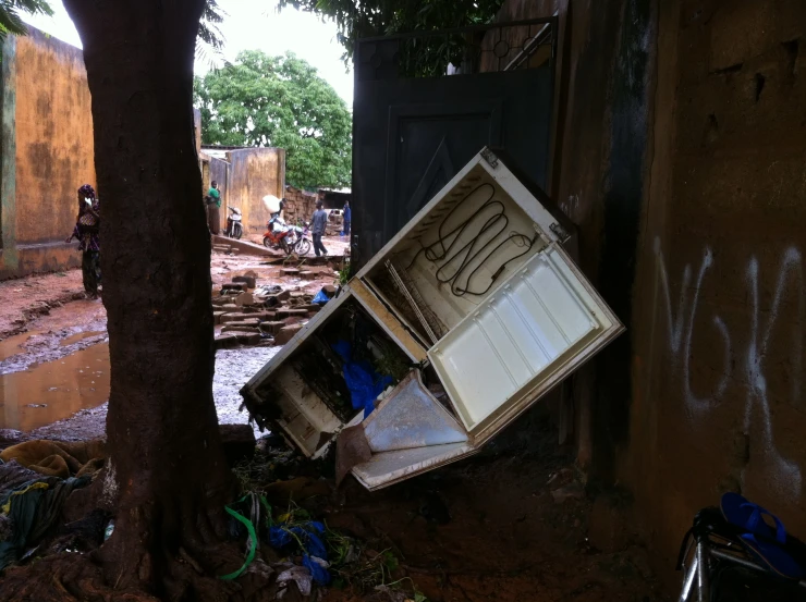 two people standing near a dirty road with an overturned cabinet on the street