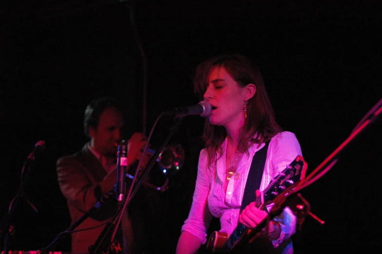 two people on stage singing while a woman plays the guitar