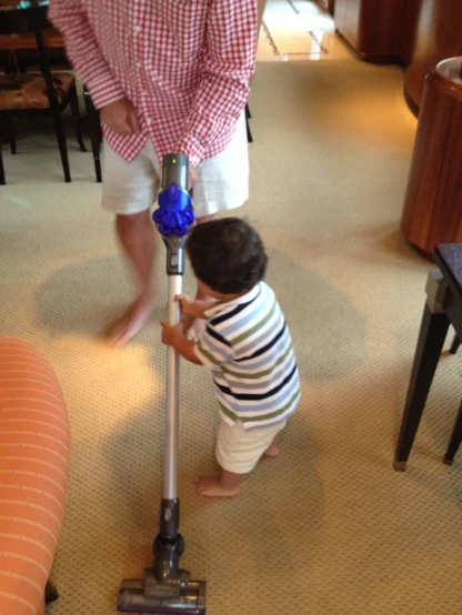 young child uses blue and red vacuum cleaner while standing in room