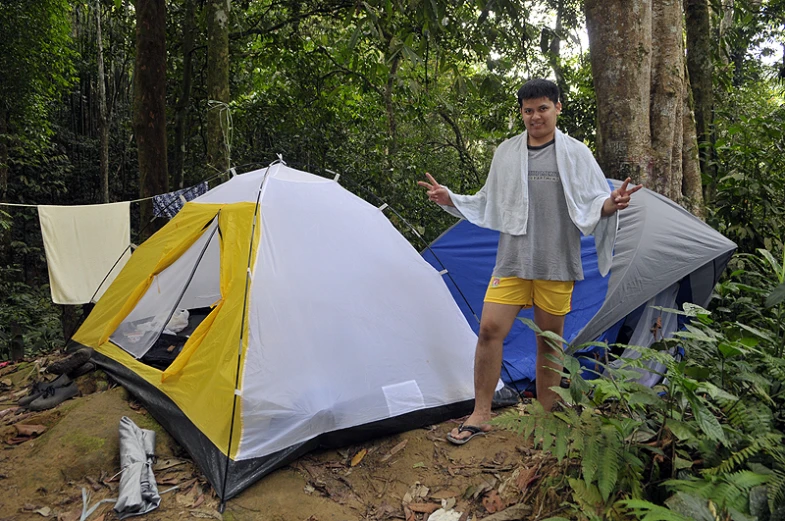 a man standing near a tent in the woods