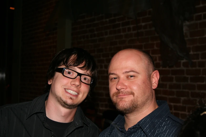 two males are posing for a po near a brick wall