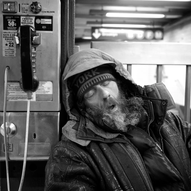 the man sleeps in front of an old pay phone