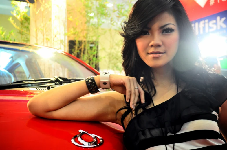 woman posing in front of a red car at a show