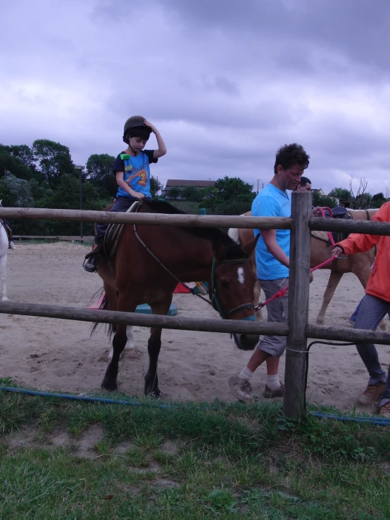 a small boy standing on a horse behind a fence