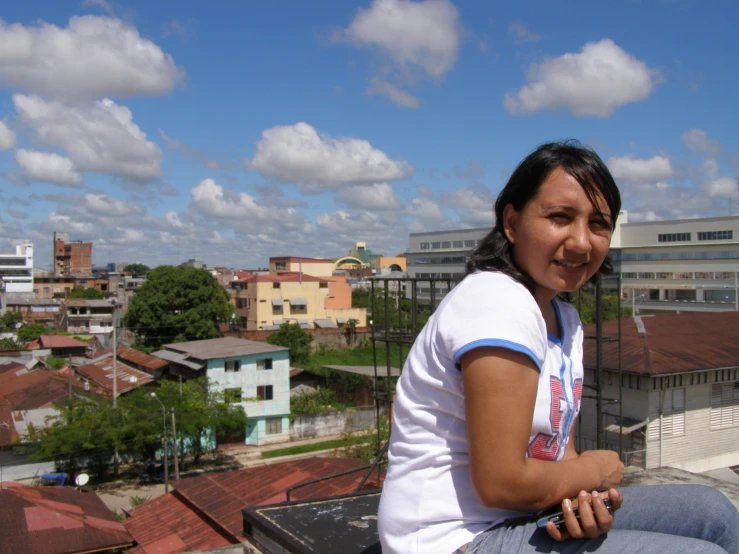 a smiling young woman sitting on the roof of a building