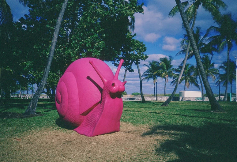 a pink snail like sculpture is shown in a park