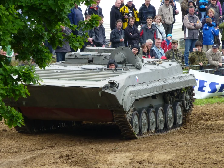 a tank in the dirt, with people watching it