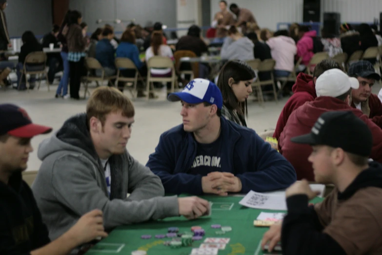 men sitting at tables playing cards with other people seated around them